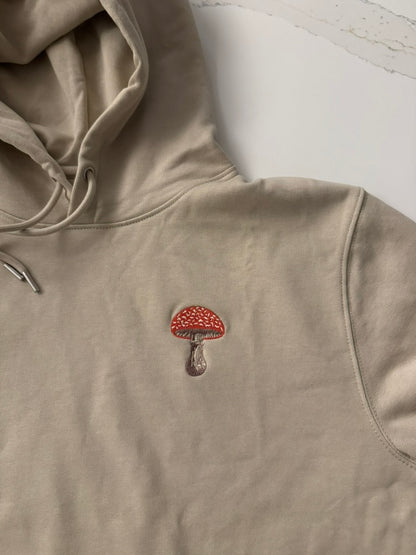 Beige hoodie with a red and brown mushroom emblem on a light background