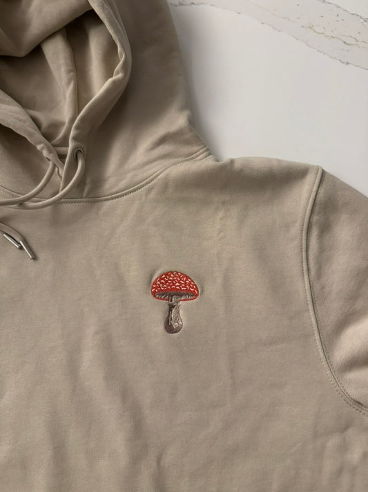 Beige hoodie with a red and brown mushroom emblem on a light background